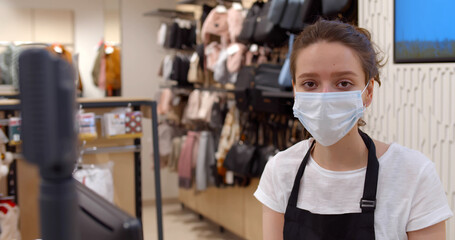 Fototapeta na wymiar Portrait of young woman seller putting on safety mask in clothing store