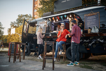 young couple flirting in front of truck with food while employee looking at them, smiling