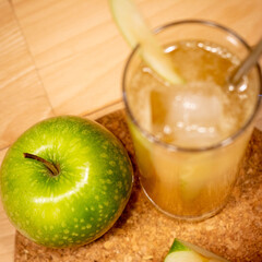 Apple and cocktail in collins glass with ice and straw and apple garnish on wood table and plant background