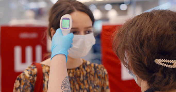 Young woman in protective mask checking temperature before entering shopping mall