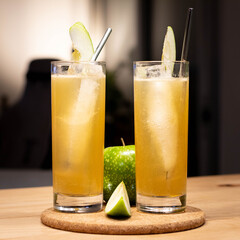 Apple and cocktail in collins glass with ice and straw and apple garnish on wood table and plant background