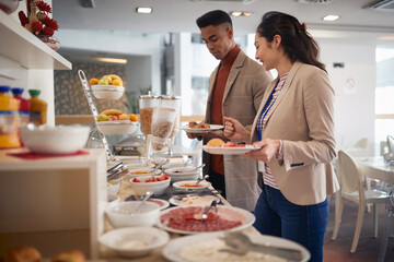 young asian female talking with afro-american male, choosing food at lunch break buffet