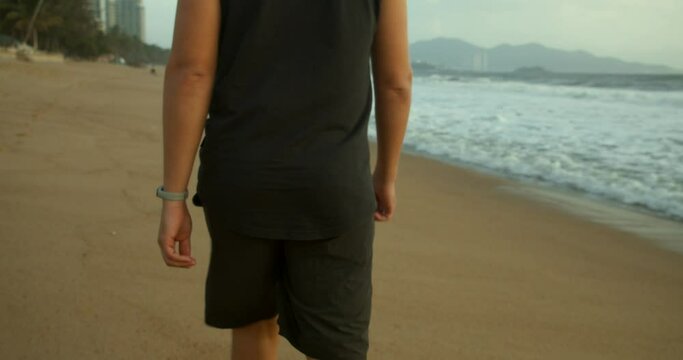 Young Caucasian Man Walking on the Sand Along the shore outdoors against the backdrop of the beautiful sea.Walk on the sand on beach at sunset against the backdrop of the sea