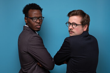 Two african and caucasian men in suit with glasses turning back being angry on their boss. Studio shot