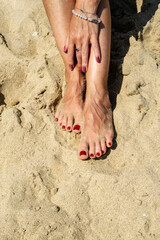 Woman legs with red pedicure relaxing on the sand. The hand strokes the leg. Summer beach