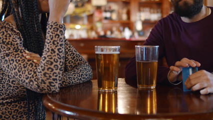 Diverse couple sitting in modern beer pub waiting for waiter to pay bill with credit card
