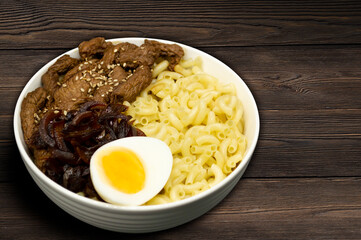 Meat with caramelized onions, egg and pasta on a wooden background