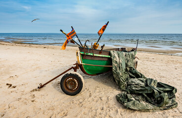 Anchored fishing boat on sandy beach near a small village of fishermen; here, at the Baltic Sea,  traditional and mighty Baltic fisheries was once successfully developed in 19-20-th centuries

