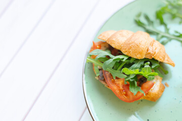 Croissant with rocket salad and vegetables on a ceramic dish on a wooden table