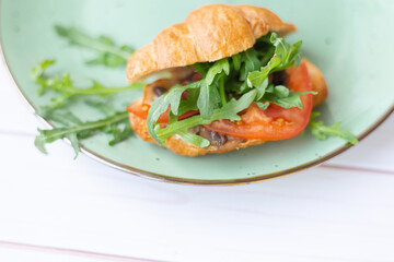 Croissant with rocket salad and vegetables on a ceramic dish on a wooden table