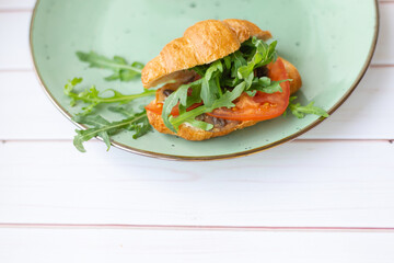 Croissant with rocket salad and vegetables on a ceramic dish on a wooden table
