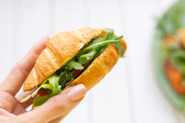 Hand holds croissant with arugula and vegetables