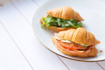 Two coissant with rocket salad and vegetables on a ceramic dish on a wooden table