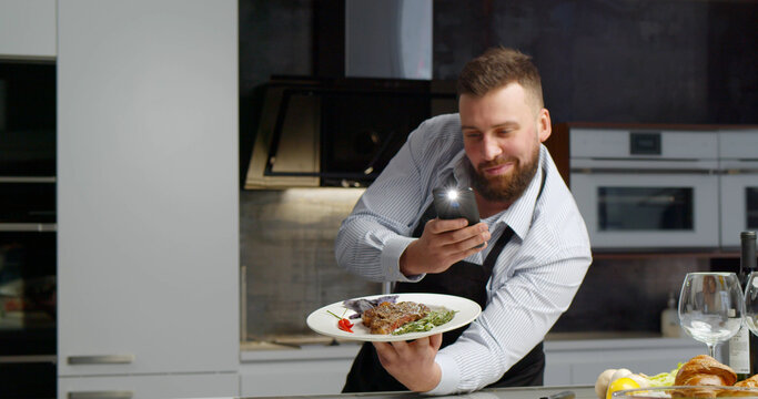 Young man taking picture of roasted steak on plate with vegetables