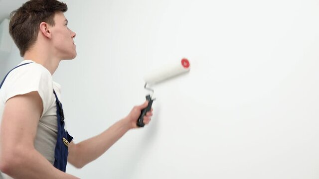 The painter paints the white walls with a paint roller