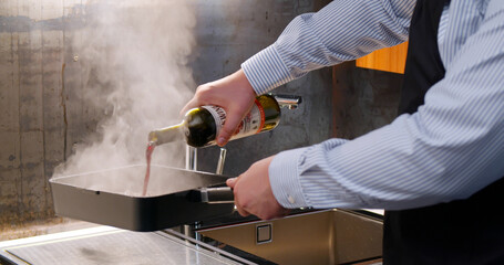 Man cook in apron frying steak on pan and adding wine at kitchen
