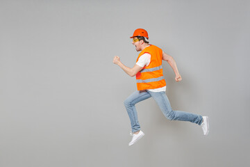 Fototapeta na wymiar Full length side view of young employee handyman man in orange vest protective hardhat jump high running isolated on grey background studio. Instruments for renovation apartment. Repair home concept.