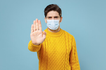 Young serious strict man 20s in yellow sweater, sterile face mask safe from coronavirus virus...