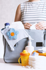 Unrecognizible pregnant caucasian woman in striped t-shirt packing big gray diaper bag to maternity...