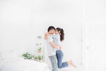 Obraz na płótnie Canvas asian lover in white room, asian man carry asian woman, htey hug and kiss together, they feeling happy and smile, honeymoon happiness