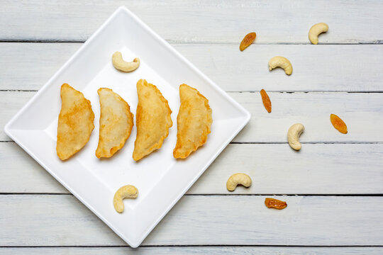 Bengali sweet - puli pitha in a white plate on wooden background with cashew nut and raisins.