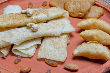 Bengali sweet - Patishapta Pitha, Malpua and Puli Pitha in a earthenware plate on wooden background with cashew nut, almonds and raisins.