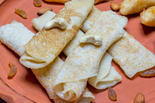 Bengali sweet - Patishapta Pitha, Malpua and Puli Pitha in a earthenware plate on wooden background with cashew nut, almonds and raisins.