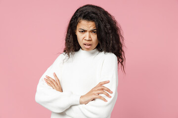 Fototapeta premium Young indignant displeased african american woman 20s curly hair in white knitted sweater look camera hold hands crossed folded isolated on pastel pink background studio portrait. Lifestyle concept.