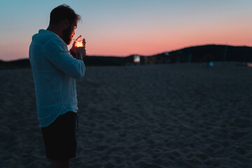 Attractive men lights a cigarette at the beach at sunset