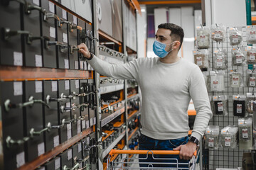 Portrait of young man wearing disposable medical mask choosing new door handles in household store