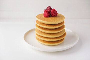 Freshly cooked soft delicious gluten free pancakes stacked on white plate, served with fresh raspberries, close up. Space for text. Healthy sweet food.