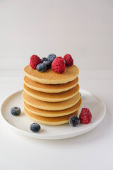 Freshly cooked soft delicious gluten free pancakes stacked on white plate, served with fresh berries, close up. Space for text. Healthy sweet food.