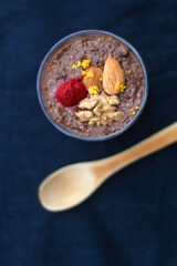 Glass of chocolate, orange and chia seed pudding with nut and raspberry topping. Top view, dark blue background.