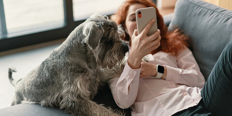 Girl shopping online with her dog on the couch using smartphone