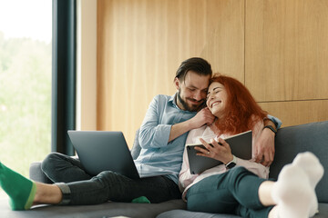 Young family couple working together, using laptop and notebook at cozy living room