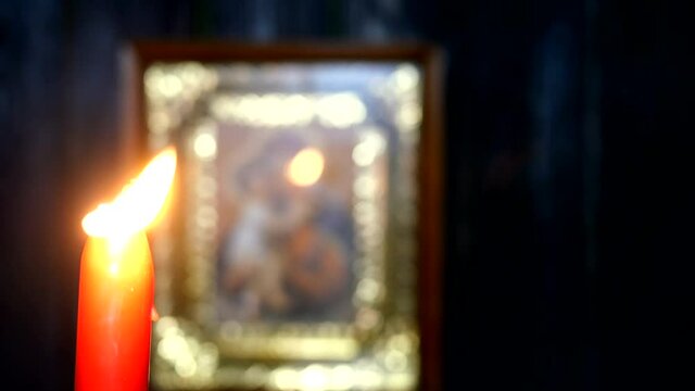 Candles are burning in dark against blurred Virgin Mary icon. Religion and spirituality. On dark wooden wall background. Close-up.