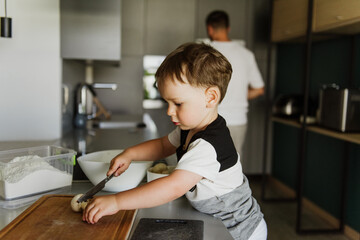 A little boy cuts mushrooms in the kitchen.
