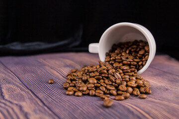 coffee beans sprinkled from a white cup on a wooden table