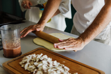 Close-up of a man's hands roll out the dough on pizza in the kitchen.