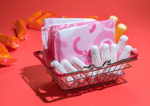 tampons and pads for feminine hygiene in a supermarket basket on a red background