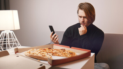 Young caucasian man having a complaint about pizza. Holding smartphone to call customer support. High quality photo