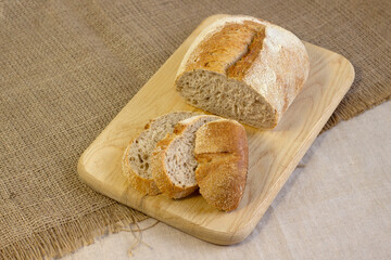 Appetizing freshly baked bread with a golden brown crust on wood cutting board a rough linen cloth close-up