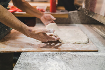Chef shaping pizza dough on wooden board, side view