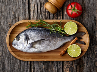 Dorado fish on the wooden  with lime, rosemary and tomato. Top view.