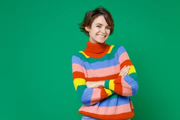 Gardinen Farbenfroh Smiling beautiful young brunette woman 20s years old wearing basic casual colorful sweater standing holding hands crossed looking camera isolated on bright green color background studio portrait.  © ViDi Studio