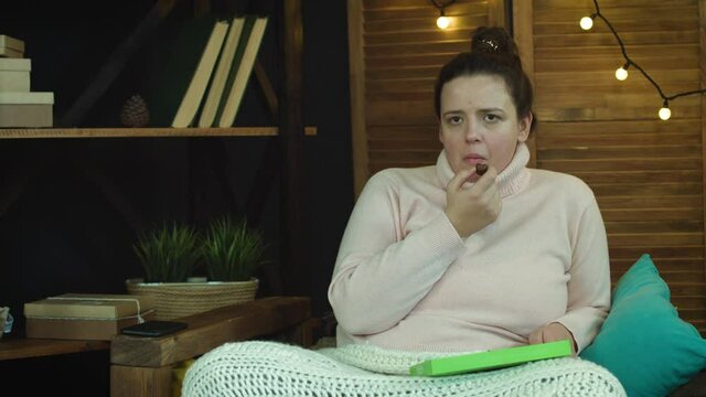 European Caucasian looking woman is watching TV eating chocolates, waiting for a 
message or call, checking her phone 