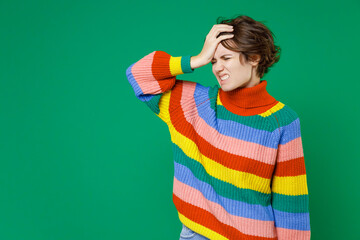 Sick exhausted tired young brunette woman 20s years old in colorful sweater standing put hand on head keeping eyes closed having headache isolated on bright green color background studio portrait.