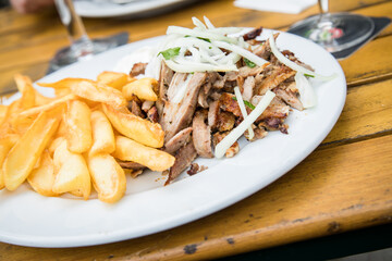 Griechisches Schweinefleisch Gyros mit Zwiebeln, Tsatsiki und Pommes auf Holz Tisch in Restaurant