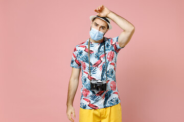 Sick tired young traveler tourist man in face mask to safe from coronavirus virus covid-19 put hand on head isolated on pink background. Passenger traveling on weekend. Air flight journey concept.
