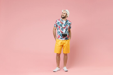 Full length funny young traveler tourist man in summer clothes hat with photo camera looking aside up isolated on pink background studio. Passenger traveling on weekends. Air flight journey concept.